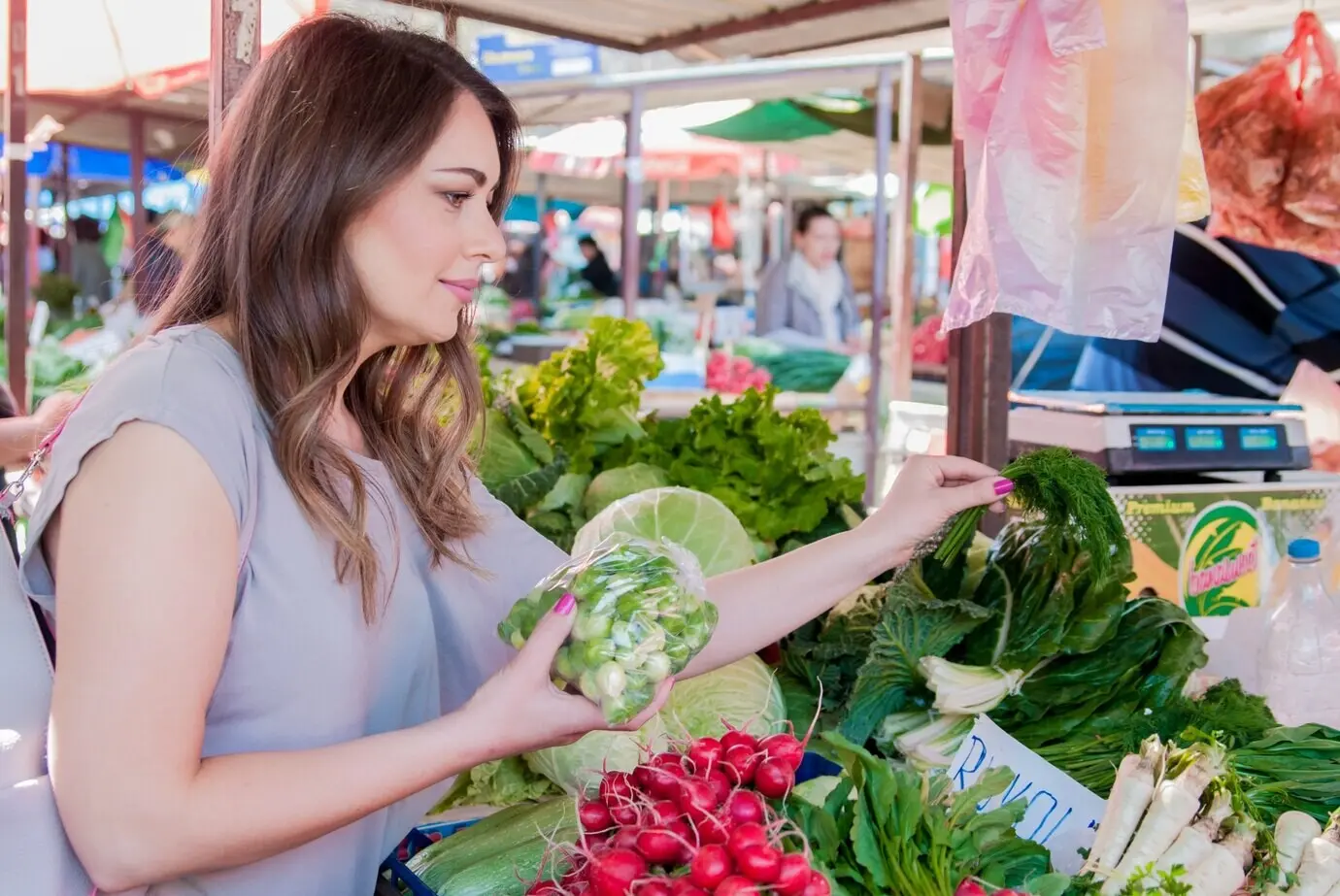 A woman shopping for fresh organic vegetables at a street market; a smiling woman with a vegetable at a market store. Concept of healthy food shopping.